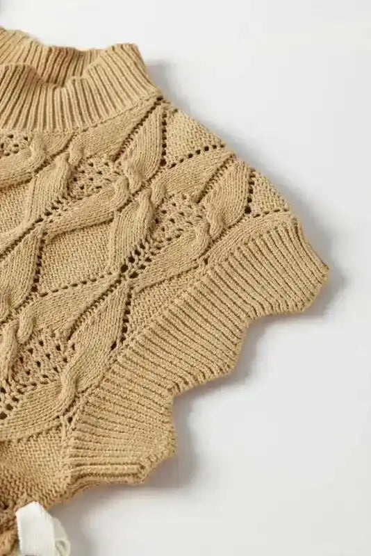 Close-up of sleeve and scalloped edge on beige high neck sweater, showcasing openwork knit pattern and ribbed finish.