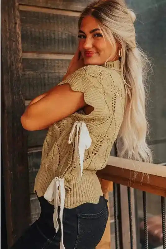 Side view of beige scalloped knit sweater with white ribbon ties, showcasing short sleeves and textured cotton blend fabric.