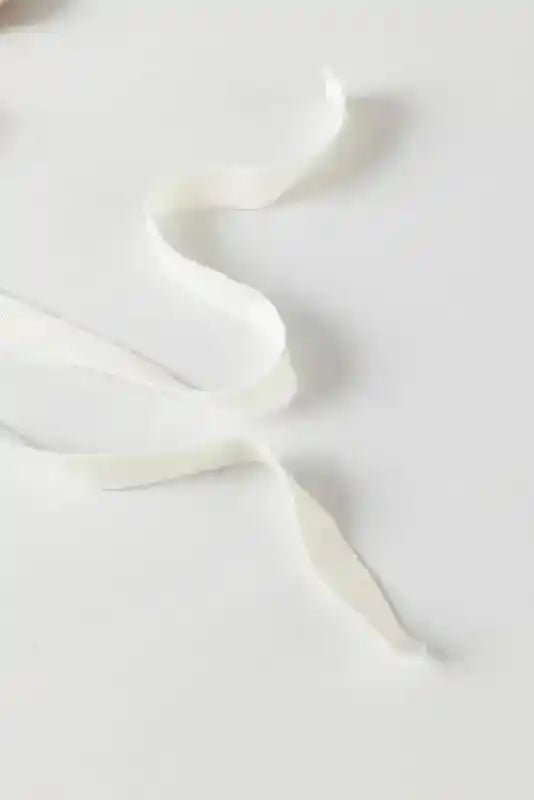 Detail of white ribbon tie used on the sides of the beige knit sweater, adding a delicate and feminine touch.