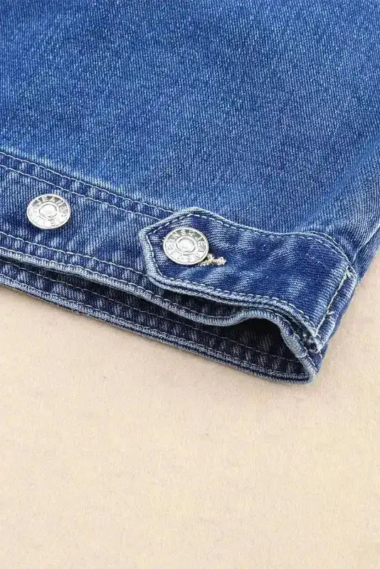 Detail of sleeve cuff on women's denim jacket with silver button accents and reinforced stitching for durability.