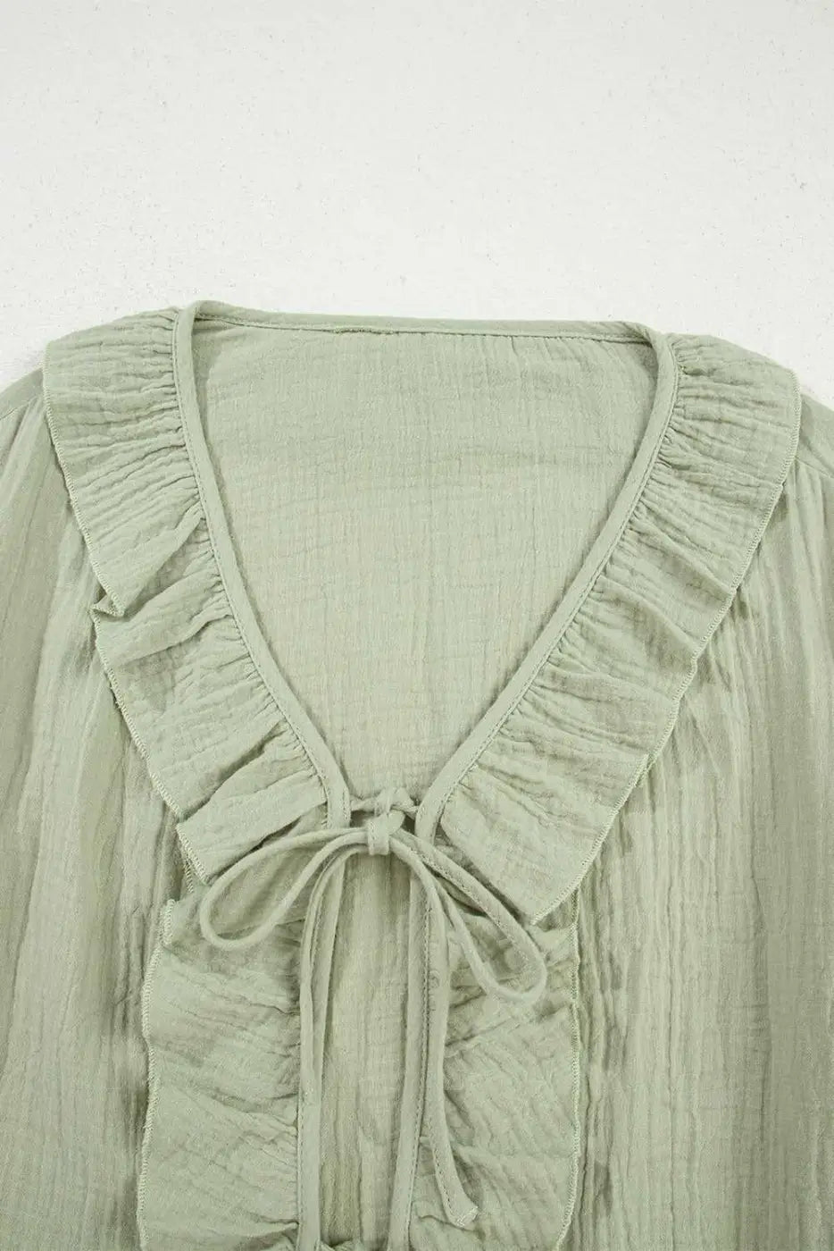 Close-up of Meadow Cotton Blouse neckline showing ruffle trim and tie detail, crafted from soft, breathable cotton fabric in solid green.