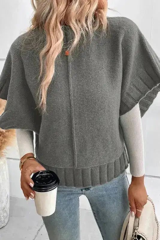 Gray batwing knit sweater layered over a long sleeve top, styled with jeans and accessorized with a coffee cup.