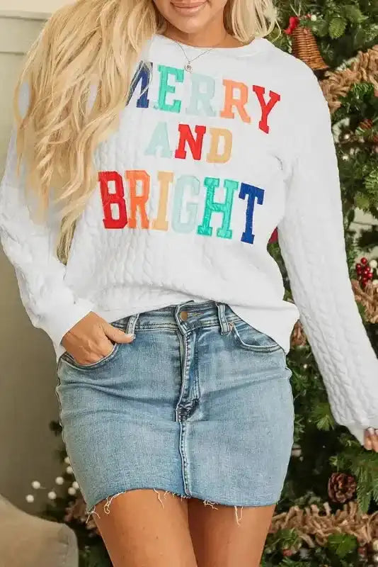 Front view of white Merry And Bright Cable Knit Sweatshirt with colorful text, styled for a cozy holiday outfit.