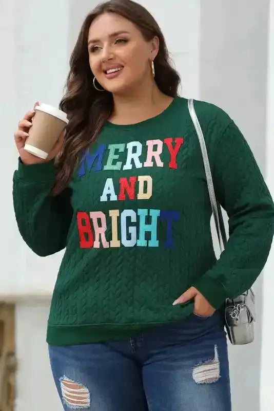 Merry And Bright Cable Knit Sweatshirt in green with colorful lettering, styled with ripped jeans for a festive casual look.