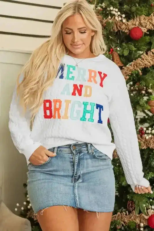 White Merry And Bright Cable Knit Sweatshirt styled with a frayed denim mini skirt, perfect for festive casual wear.