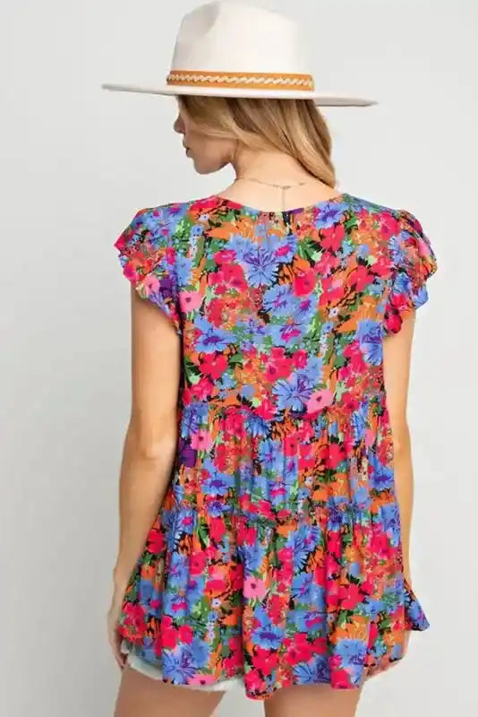 Back view of floral babydoll top for women with tiered layers and flutter sleeves, styled with a hat for a relaxed summer vibe.