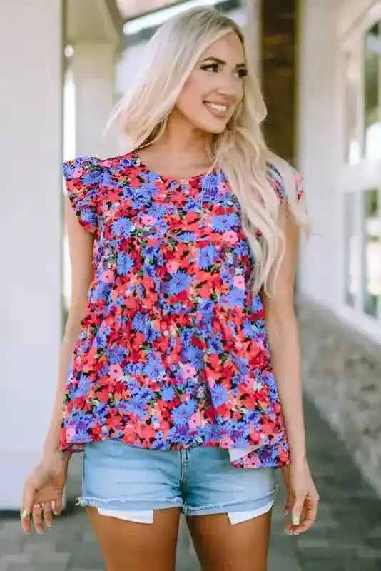 Smiling model wearing floral babydoll top for women with bright floral print and tiered silhouette, styled for a casual summer day.