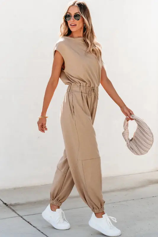 Relax relax in a beige sleeveless jogger jumpsuit with gathered ankle cuffs and white sneakers