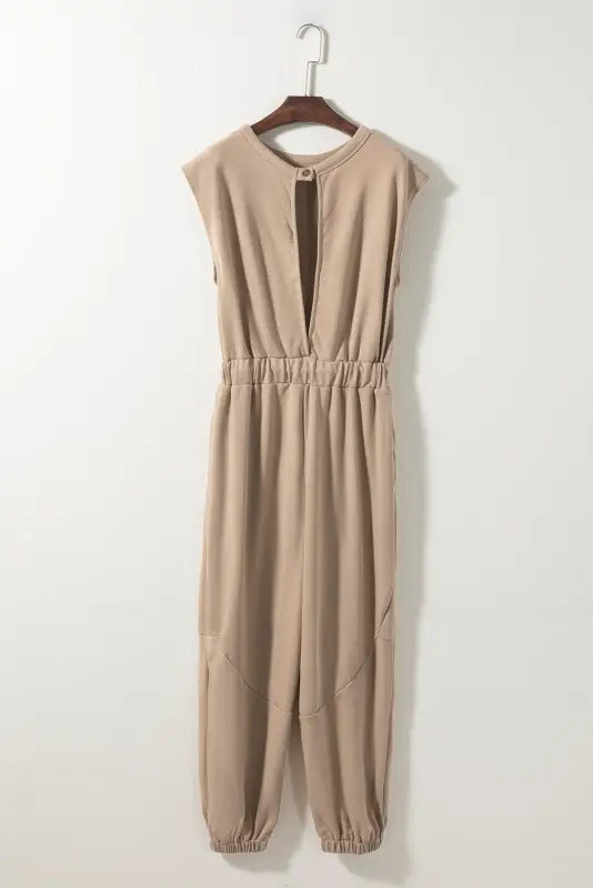 Beige relax jogger jumpsuit with elastic waist and tapered legs on a wooden hanger