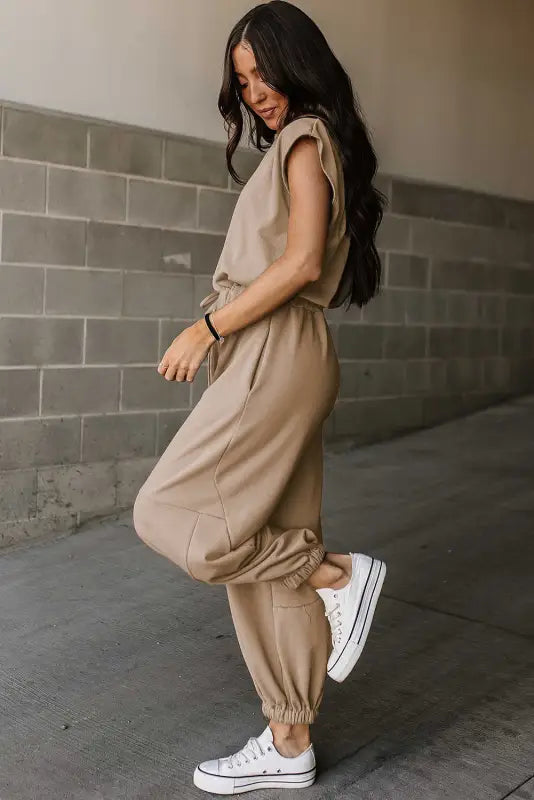 Woman in beige open back jogger jumpsuit and white sneakers, perfect for relax relax style