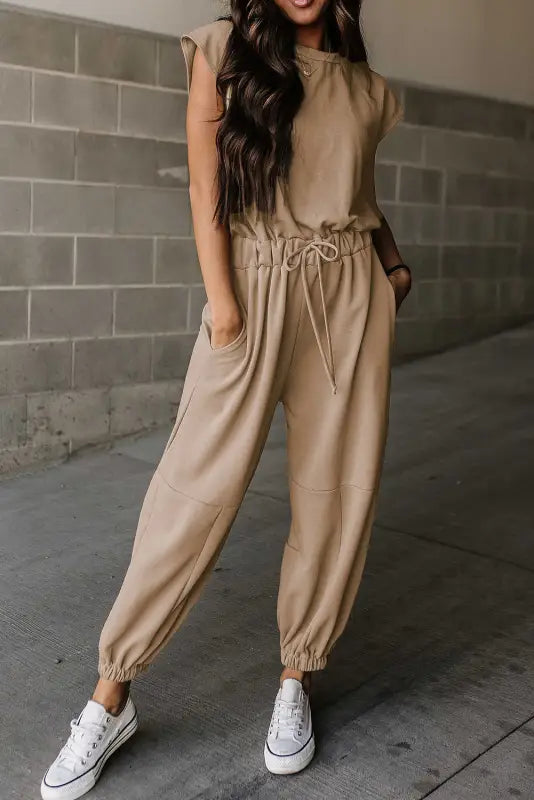 Open back drawstring jogger jumpsuit: beige jumpsuit with tapered legs, paired with white sneakers