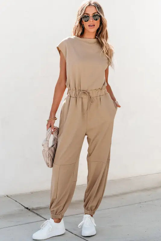 Open back drawstring jogger jumpsuit: beige, cinched waist, loose pants, white sneakers, sunglasses