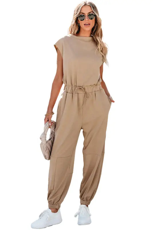 Woman wearing a beige sleeveless jogger jumpsuit with gathered waist and ankle cuffs