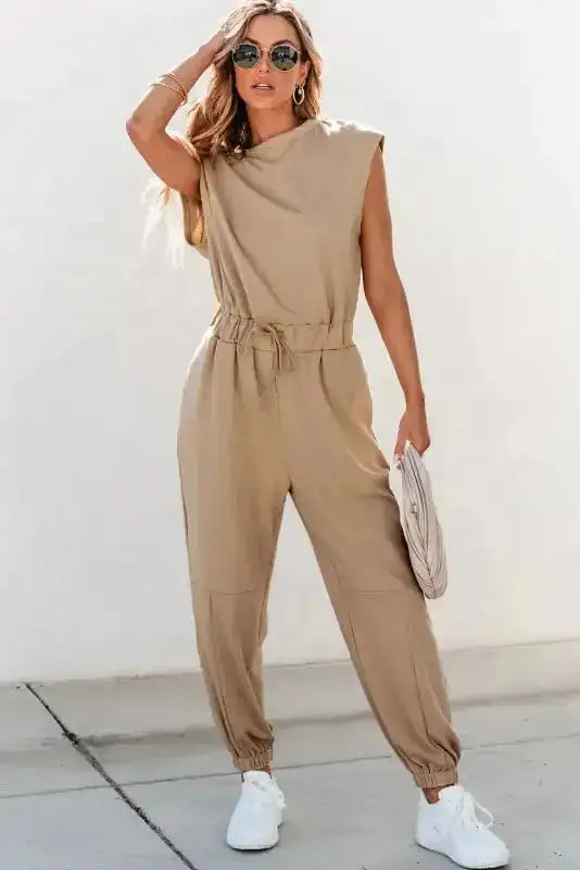 Stylish beige jogger jumpsuit with open back and cap sleeves, paired with white sneakers for a relaxed look.