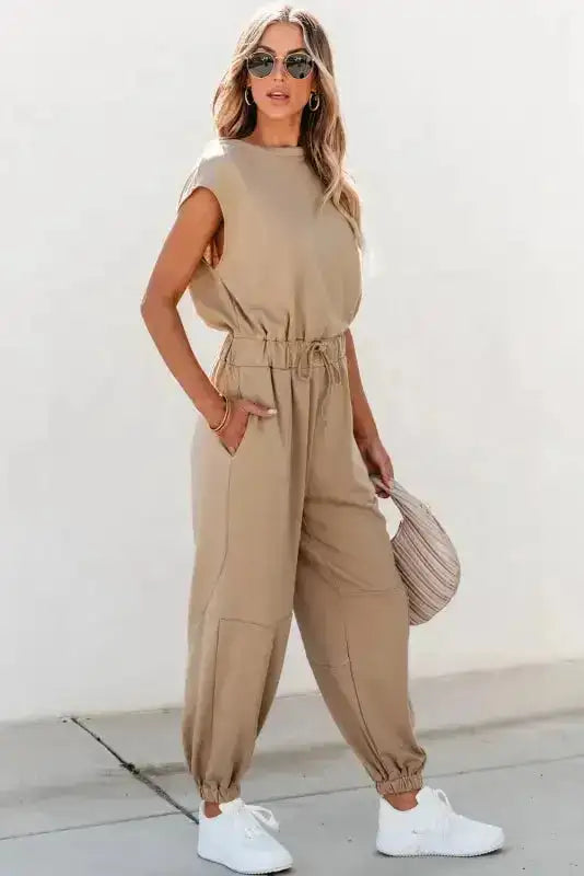 Beige women’s jogger jumpsuit with open back and elastic cuffs, styled for modern casual wear.