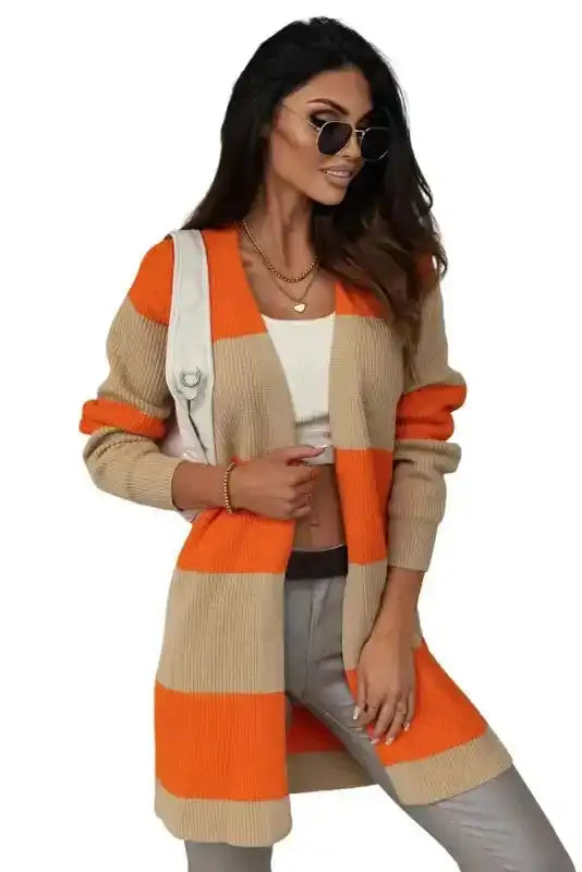 Orange cardigan in ribbed knit with beige colorblock design, worn open over a crop top and pants for a trendy daily outfit.