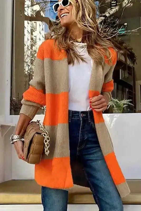 Trendy orange cardigan with colorblock knit design, worn with jeans and white top for a stylish fall-to-winter transition outfit.