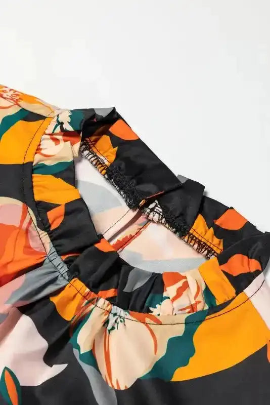Close-up of ruffled neckline and stitching on orange floral blouse, showcasing soft fabric and detailed craftsmanship.