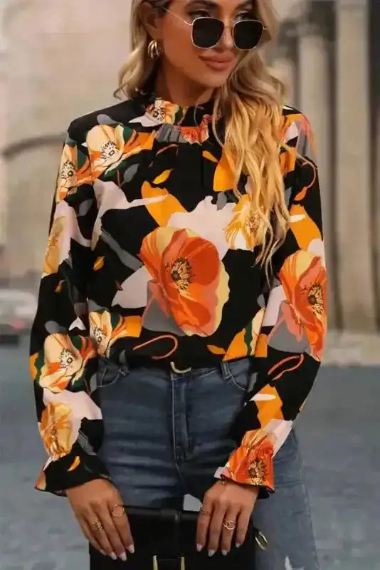 Chic floral blouse with orange and yellow blooms, long sleeves, and high neck, styled for casual streetwear.