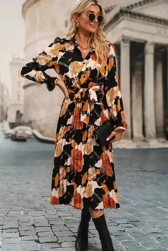 Model styling Orange Floral Tie Neck Dress with clutch and boots, highlighting its versatility for daily or travel wear.