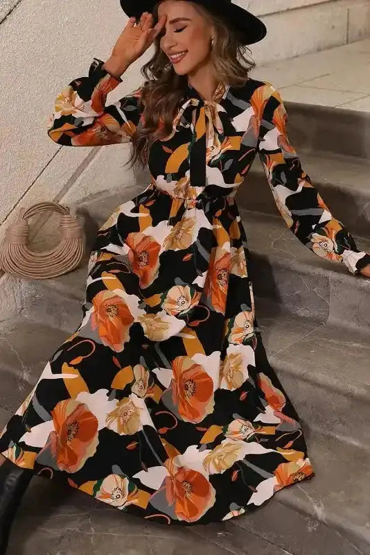 Relaxed pose in orange floral tie neck dress with long sleeves, highlighting the A-line silhouette and vibrant print.