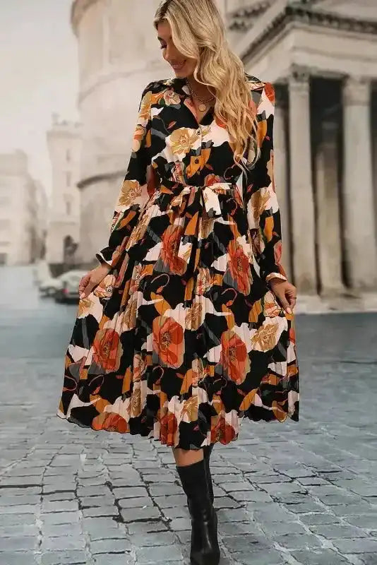 Model twirling in Orange Floral Long Sleeve Dress with pleated skirt and tie waist, perfect for feminine and elegant occasions.