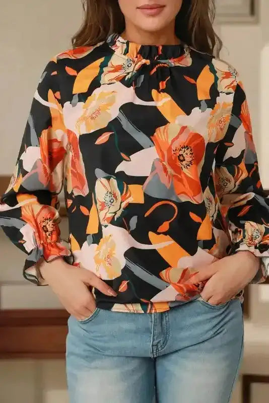 Orange floral print blouse with ruffled neckline and cuffs, paired with light denim for a soft, feminine look.