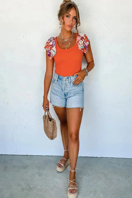 Full-body view of woman wearing ladies orange ribbed knit bodysuit with ruffled sleeves, styled with denim shorts and espadrilles for summer fashion.