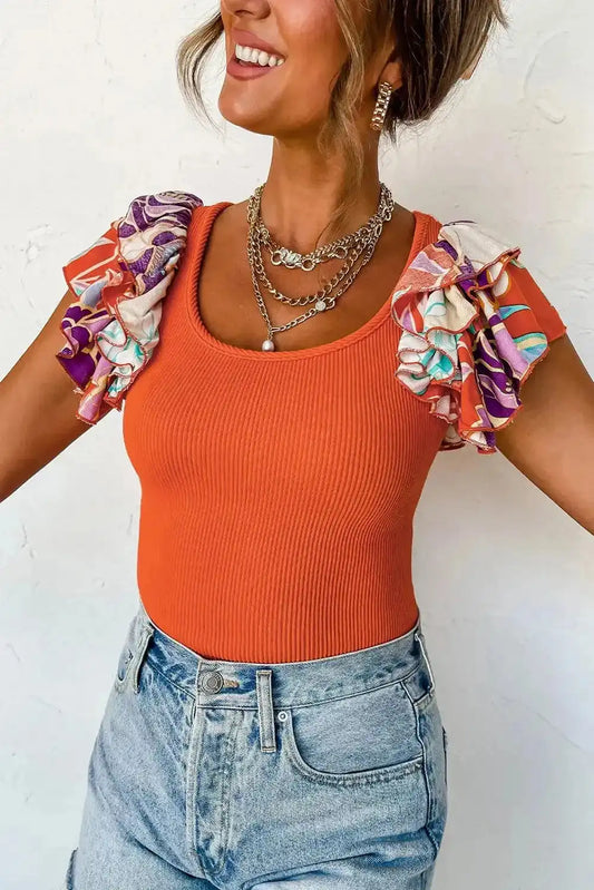 Orange ribbed knit bodysuit featuring vibrant ruffled sleeves in floral print, paired with denim for a casual yet stylish outfit.