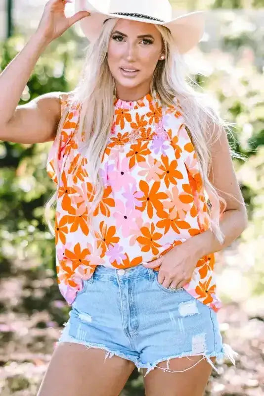 Orange smocked floral top with ruffled sleeves styled with denim shorts and a white hat. Lightweight summer blouse from FashionFitz.