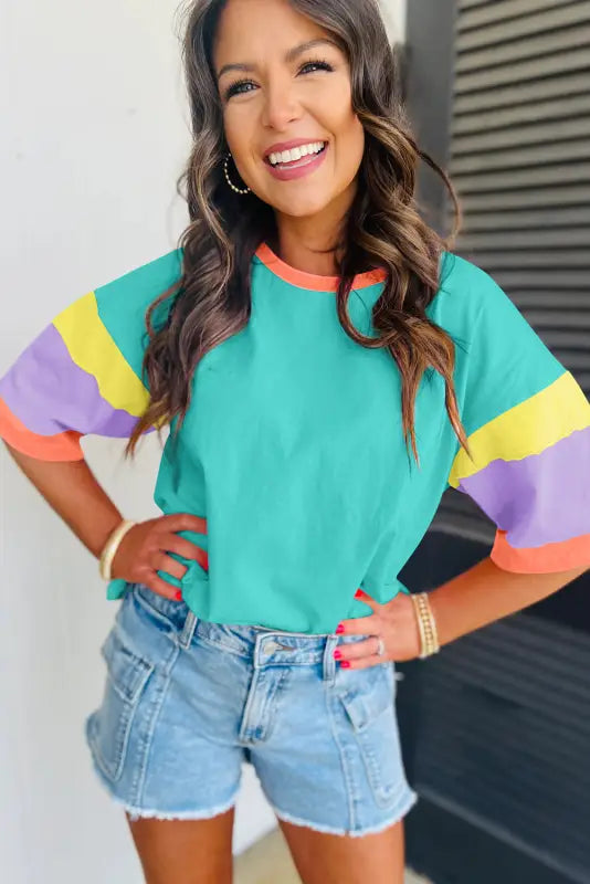 Woman in relax relax oversized stitched turquoise top with striped sleeves and denim shorts