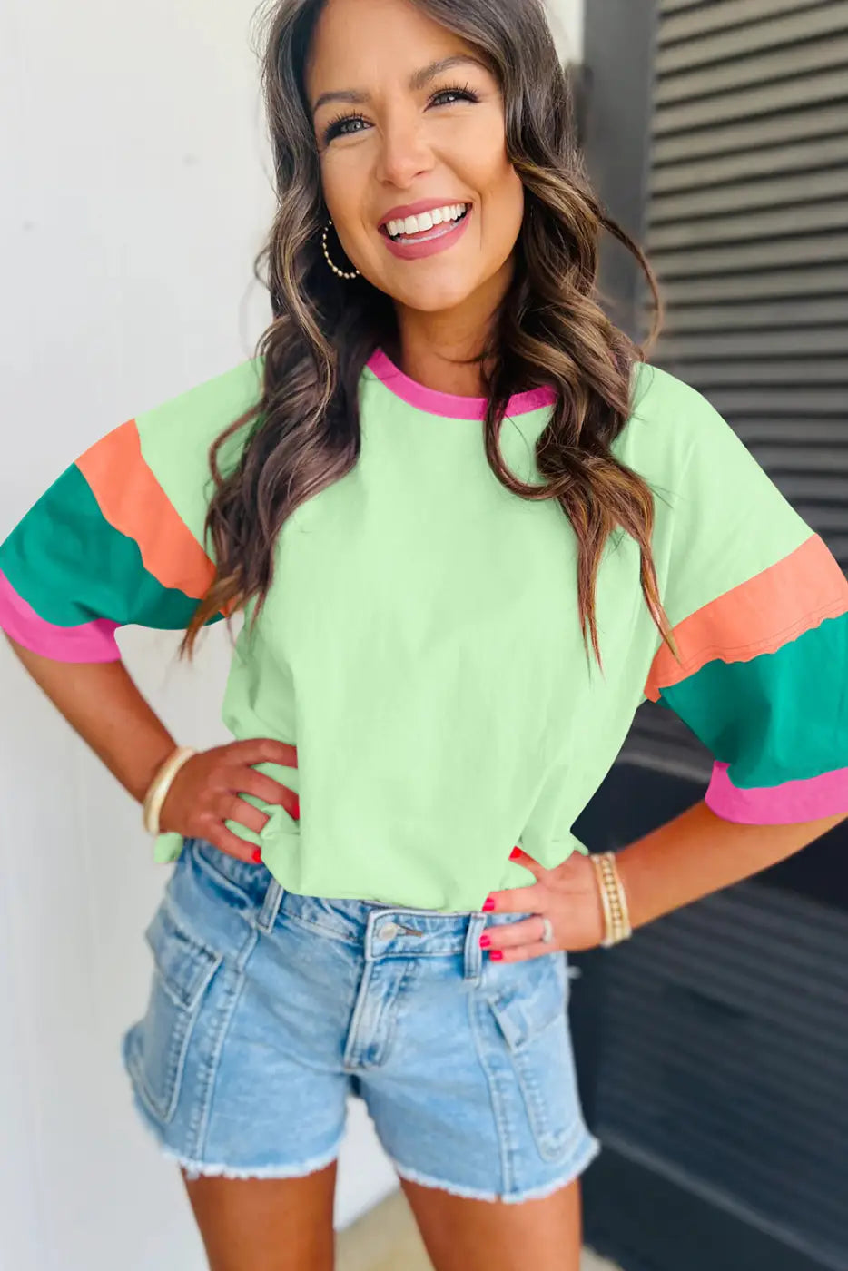 Woman in colorful striped oversized stitched top, denim shorts, smiling brightly. Relax relax relax