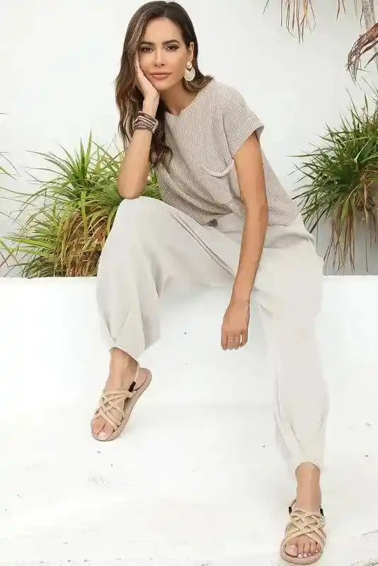 Model seated in Pale Khaki Patch Pocket Short Sleeve Sweater paired with loose white pants and sandals for a relaxed outfit.