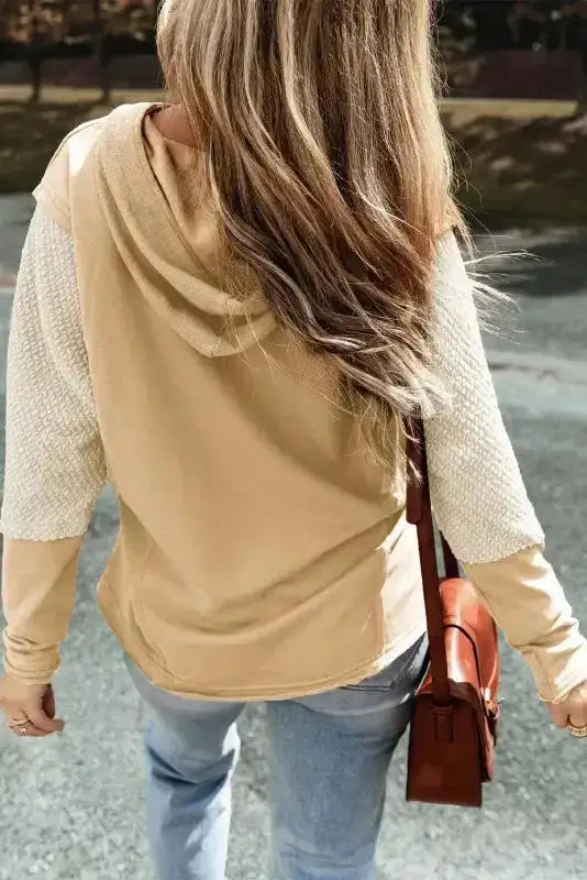 Back view of beige Patchwork Hoodie with textured knit sleeves and oversized fit, paired with jeans for a relaxed look.