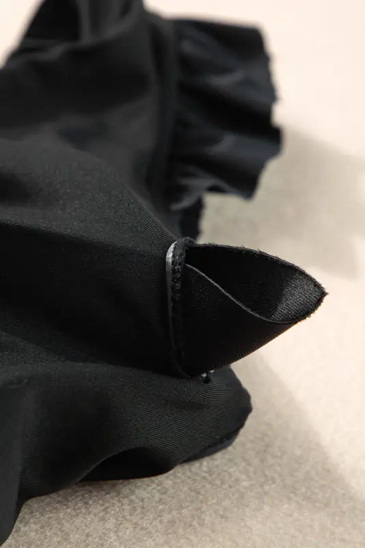 Black fabric umbrella with pointed tip and folded sections shown next to one piece bathing suit