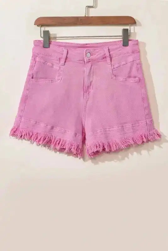 Flat lay of pink mid rise denim shorts with frayed hem, made from stretch cotton for casual summer wear.