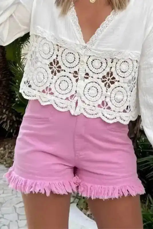 Front view of pink mid rise denim shorts with frayed hem, paired with a white lace blouse for a casual summer look.