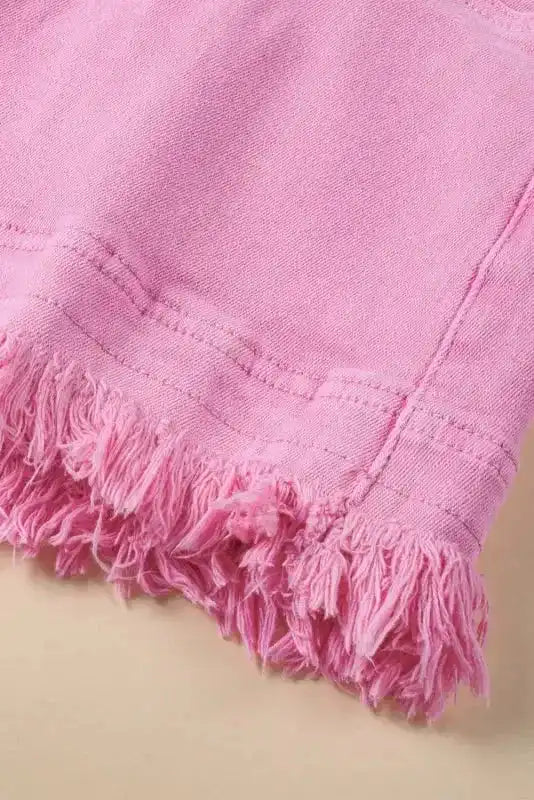 Close-up of frayed hem detail on pink mid rise denim shorts, highlighting the textured finish and stretch cotton fabric.