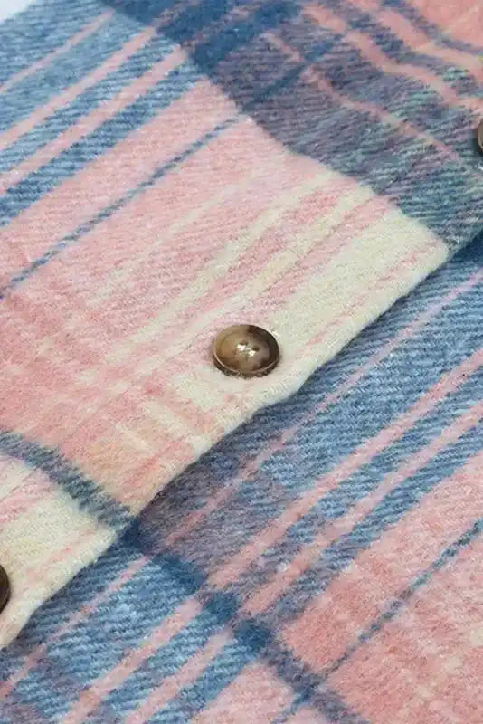 Close-up of button detail on stylish plaid shacket with flap pockets, showcasing soft fall fabric and pink-blue check pattern.