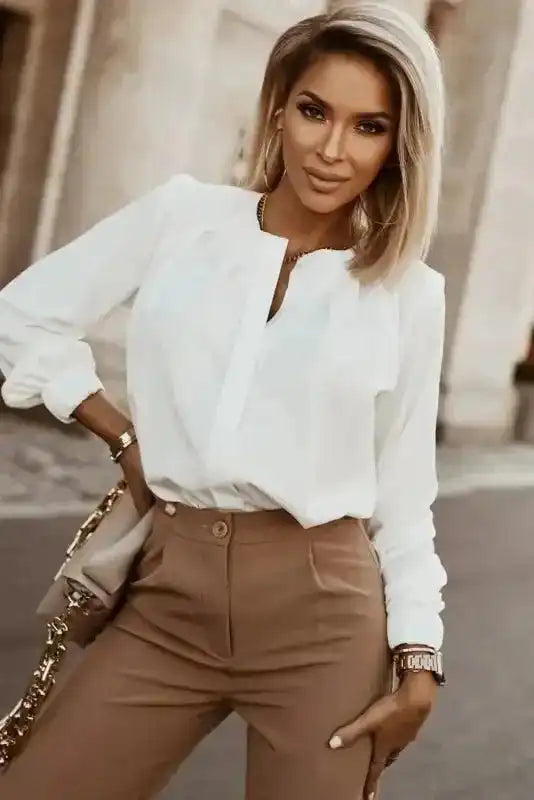 White Pleated Neck Stretch Cuff Shirt styled with tan trousers. A refined women's blouse for elegant fall fashion.