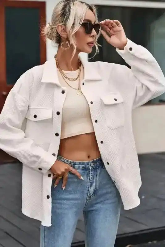 Side view of a woman adjusting sunglasses while wearing a white textured plus size jacket, paired with high-waisted jeans.