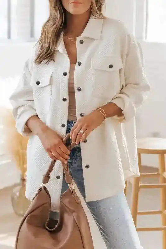 Model wearing a white textured plus size jacket with black buttons, styled casually with jeans and a neutral top for winter fashion.
