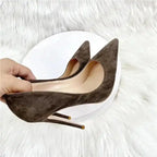 Close-up of brown suede stiletto pumps held in hand, emphasizing the shoe's craftsmanship and luxurious material.