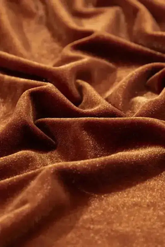 Rich chestnut velvet fabric with soft drape and sheen, used in elegant swing dress with frilled neck and puff sleeves.