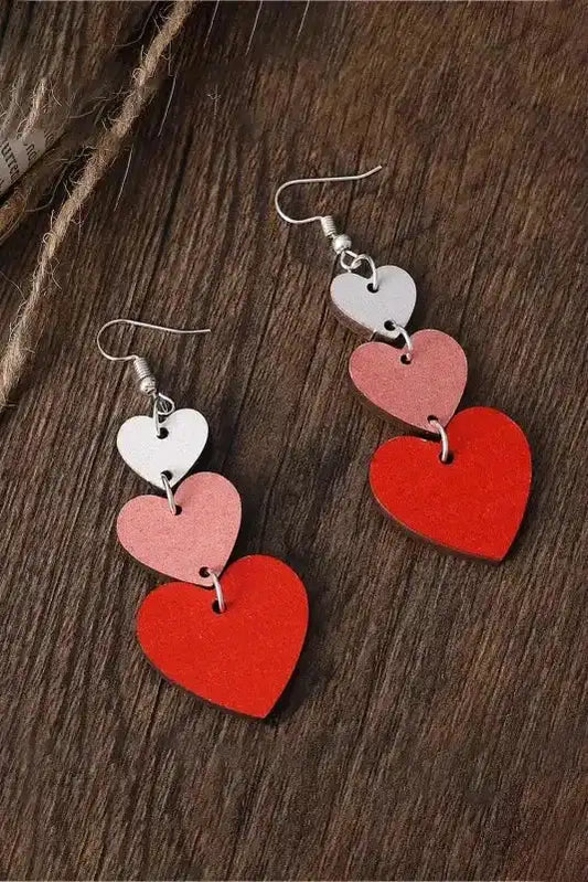 Red Heart Tiered Dangle Earrings – Valentine’s Day Edition with layered heart shapes in red, pink, and white displayed on a wooden surface.