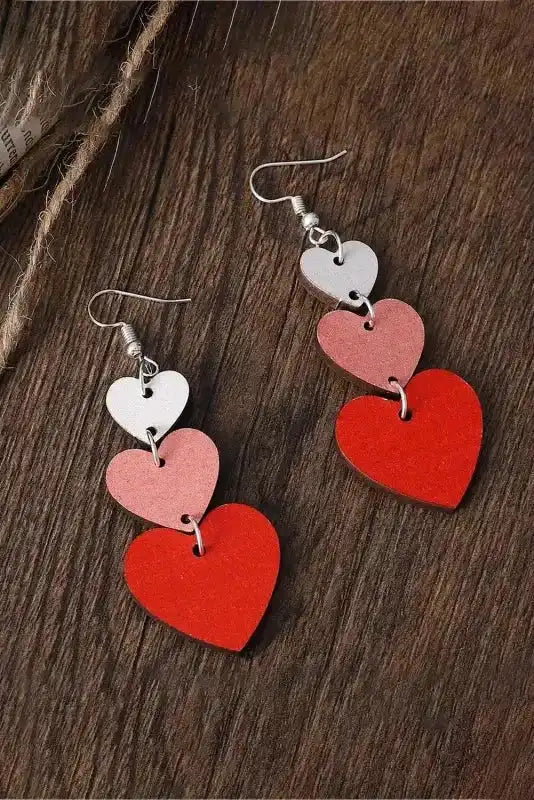Red Heart Tiered Dangle Earrings – Valentine’s Day Edition with layered heart shapes in red, pink, and white displayed on a wooden surface.