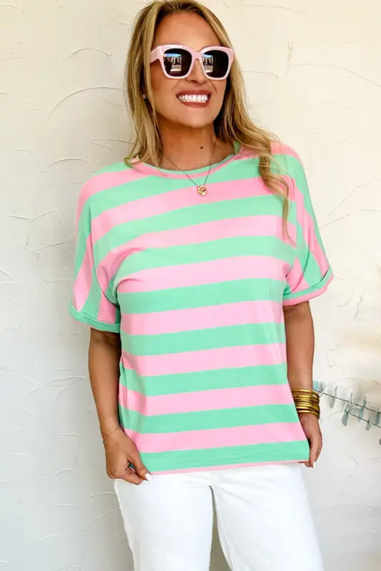 Smiling person wearing sunglasses and a striped pink and green relaxed elegance tee