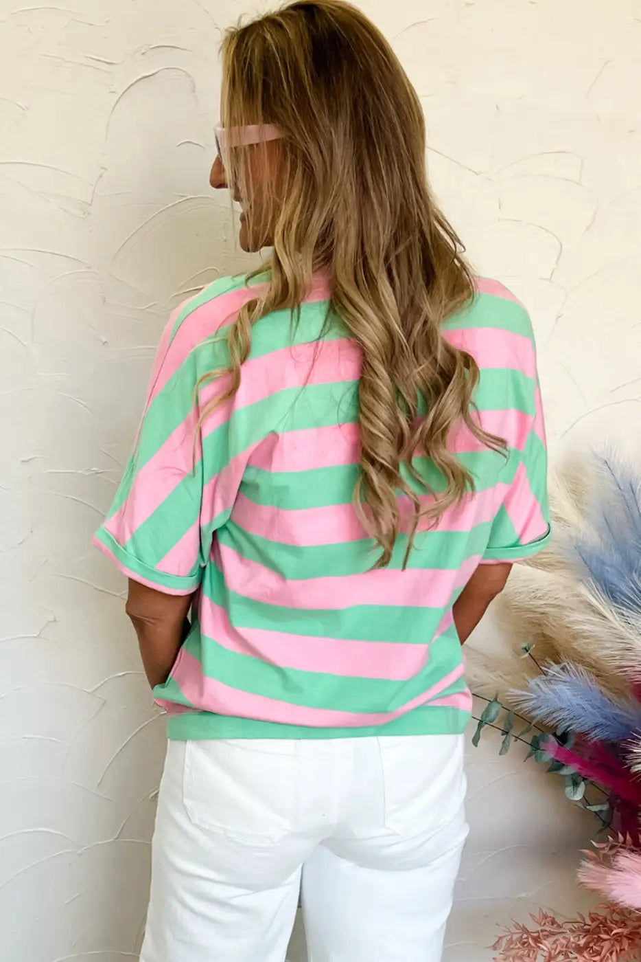 Woman wearing relaxed elegance tee: pink and green striped shirt with white pants