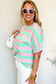 Smiling blonde woman in relaxed elegance tee, pink and green stripes, white sunglasses