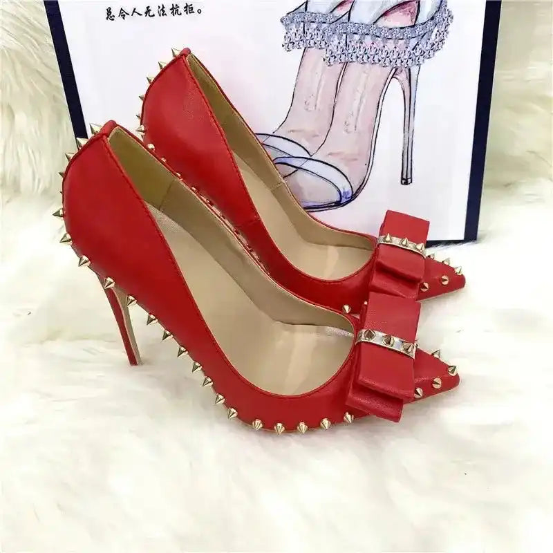 Red Riviera Bow Court Heels with gold spikes and bow detail, displayed against a fashion-themed background for stylish appeal.